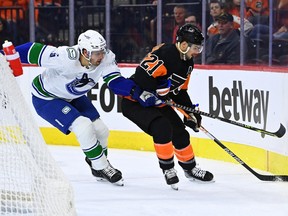 Vancouver Canucks defenseman Tucker Poolman reaches across Philadelphia Flyers left wing Scott Laughton as he collects the puck in the first period at Wells Fargo Center on Oct. 15, 2022.