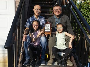 Andy Yan (right) with his nieces Natalie Yan (in pink), 9, Emily Yan (in green), 7, and his dad Howard Yan, look over artifacts from the Yan Society in Vancouver, BC Thursday, October 13, 2022. The society was founded by Andy's great-grandfather Charlie, who is in the framed photo.