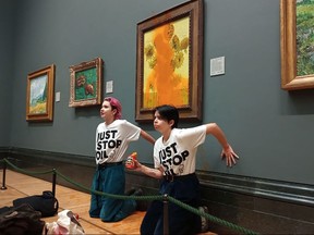 A handout picture from the Just Stop Oil climate campaign group shows activists with their hands glued to the wall under Vincent van Gogh's "Sunflowers" after throwing tomato soup on the painting at the National Gallery in central London on Oct. 14, 2022.
