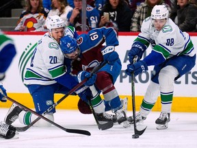 Colorado Avalanche right winger Martin Kaut (61) loses the puck to Vancouver Canucks center Nils Aman (88) as he collides with Vancouver Canucks center Curtis Lazar (20) during the first period of an NHL hockey game Wednesday, Nov. 23, 2022, in Denver.