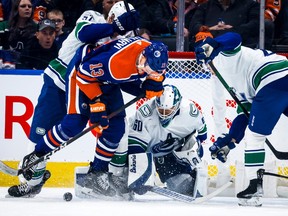 Vancouver Canucks goalie Collin Delia, centre, looks on as Edmonton Oilers forward Jesse Puljujarvi, left, is checked during first period NHL hockey action in Edmonton, Friday, Dec. 23, 2022.