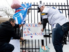 Football fans tape a sign to a fence during a vigil Tuesday, Jan. 3, 2022, outside the University of Cincinnati Medical Center where Bills safety Damar Hamlin lies in critical condition, after suffering a cardiac arrest during the Monday, Jan. 2 game against the Bengals, in Cincinnati.