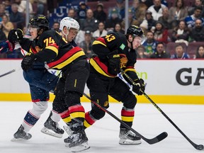 Vancouver Canucks defenseman Ethan Bear (74) checks Columbus Blue Jackets forward Patrik Laine (29) as defenseman Quinn Hughes (43) collects the loose puck during the second period at Rogers Arena Jan.  27, 2023.