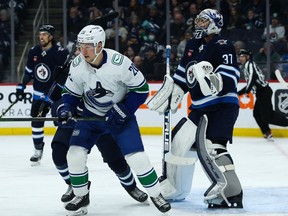 Vancouver Canucks forward Curtis Lazar, left, and Winnipeg Jets goalie Connor Hellebuyck look for the puck at the Canada Life Centre on Dec 29, 2022, in Winnipeg.