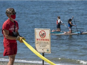 A lifeguard puts up caution tape and a warning sign alerting beach-goers the water in the area around Sunset Beach is unfit for swimming in Vancouver, BC, August, 9, 2020.