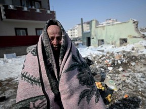 A resident stands covered with a blanket in front of his collapsed building as rescue teams carry out search operations at Elbistan district of Kahramanmaras on February 11, 2023, after a 7.8-magnitude earthquake struck the country's southeast earlier in the week. - The death toll from a catastrophic earthquake that hit Turkey and Syria climbed to more than 25,000 on Saturday, as rescuers worked in freezing weather to find people alive. (Photo by OZAN KOSE / AFP)