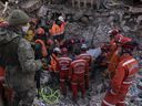 A Turkish soldier, left, watches as rescue workers of the search and rescue unit of the Turkish Gendarmerie General Command, JAK, work to pull 23-year-old Huseyin Seferoglou from the rubble of a collapsed building in Antakya, Turkey, on Sunday, Feb. 12, 2023.