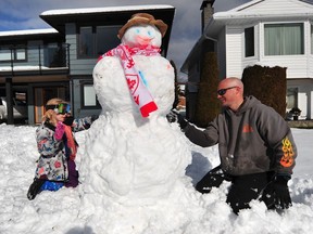 Jason Phillips and his daughter work on a snowman in the front yard of his North Vancouver home on Sunday.