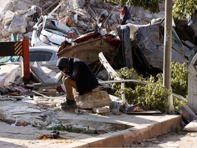 A man sits on rocks with hands on his face surrounded by rubble following the earthquake in Hatay, Turkey, on Feb. 9.