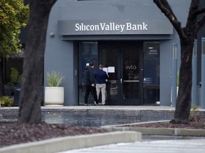 A man puts a sign on the door of the Silicon Valley Bank as an onlooker watches at the bank's headquarters in Santa Clara, Calif., on March 10, 2023.