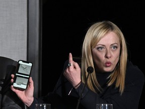 Italy's Prime Minister, Giorgia Meloni shows on her smartphone a picture, sent by European Union border agency Frontex, of the boat that sank off Cutro last February 26, killing at least 72 migrants, during a press conference on March 9, 2023 following a weekly Cabinet meeting at the town hall of Cutro, Calabria region, near the site of a deadly shipwreck where at least 72 migrants died on February 26, a symbolic gesture for Italy's far-right, openly anti-migrant government. (Photo by Tiziana FABI / AFP)