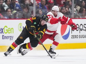 Vancouver Canucks' Quinn Hughes skates with the puck in front of Detroit Red Wings' Pius Suter  during the second period of an NHL hockey game in Vancouver, on Monday, February 13, 2023.