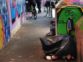 VANCOUVER, BC., March 28, 2023 - A woman shelters in a garbage bag as Vancouver police and city workers help to remove tents from the sidewalk on E Hastings St. (NICK PROCAYLO/PNG)