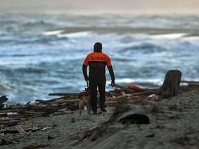 A police officer and his dog patrol the beach where debris of a shipwreck washed ashore after a boat carrying migrants sank off Italy's southern Calabria region on February 26, 2023. 59 migrants died after their overloaded boat sank in stormy seas.
