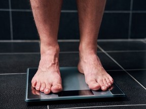 Male feet on the scale in the black tiled bathroom