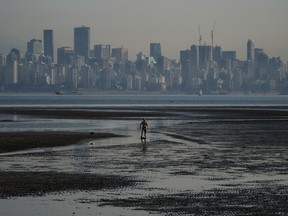 A man jumps on a skimboard while riding on tidal pools at Spanish Banks as smoke from wildfires hangs over Vancouver's downtown core on Oct. 6, 2022.