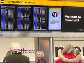 In this file photo, people stand near an arrivals board which displays a message warning users of terminal 5 about industrial action by Border Force staff at Heathrow Airport, near London, Britain, Dec. 23, 2022.