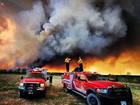 Firefighters stand on a Kamloops Fire Rescue truck at a wildfire near Fort St. John earlier this month.