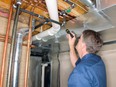 Building maintenance man examines pipes with flashlight