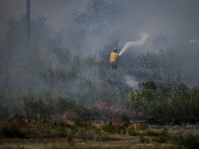 A firefighter directs water on a grass fire on an acreage behind a residential property in Kamloops, British Columbia, Monday, June 5, 2023. For the first time this year, air quality advisories are posted for part of Vancouver Island and a large section of the Lower Mainland as smoke from several wildfires wafts over the region.