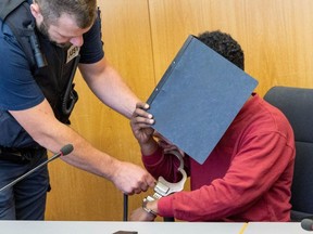 A court official, left, removes the handcuffs from the defendant, who is covering his face with a file folder, in the hearing room of the Regional Court in Ulm, Germany, Tuesday, July 4, 2023.