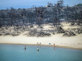 A woman enters the sea from a beach where wildfires destroyed the woods, at Glystra near the village of Gennadi in the southern part of the Greek island of Rhodes, on July 27, 2023.