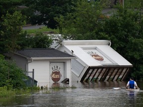 Buildings are seen upended on a riverbank as a man paddles a kayak through floodwater following a major rain event in Halifax on Saturday, July 22, 2023.