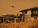 A helicopter equipped to respond to wildfires flies past homes in the Wilden neighbourhood near Knox Mountain after RCMP officers enforced a new evacuation order, in Kelowna, B.C., Friday, Aug. 18, 2023.