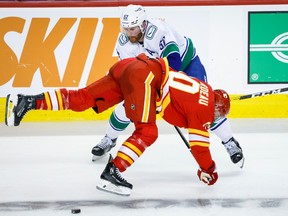 Vancouver Canucks' Matt Irwin, left, is checked by Calgary Flames forward Jonathan Huberdeau during second period NHL preseason hockey action in Calgary, Sunday, Sept. 24, 2023.