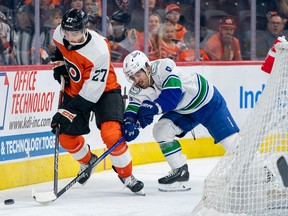 Philadelphia Flyers' Noah Cates (27) battles for the puck with Vancouver Canucks' Conor Garland (8) during the second period on Tuesday, Oct. 17, 2023, in Philadelphia.
