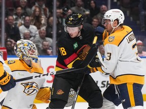 Vancouver Canucks' Sam Lafferty, centre, scores a goal against Nashville Predators goalie Kevin Lankinen, left, as the puck bounces off his helmet while Jeremy Lauzon, right, watches during the first period on Tuesday at Rogers Arena.