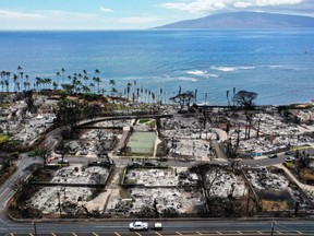 In an aerial view, a recovery vehicle drives past burned structures and cars two months after a devastating wildfire on October 09, 2023 in Lahaina, Hawaii.