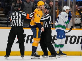 Nashville Predators right wing Michael McCarron (47) is restrained by referees has he is given a penalty unsportsmanlike behavior during the first period of an NHL hockey game against the Vancouver Canucks, Tuesday, Dec. 19, 2023, in Nashville, Tenn.