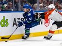 Vancouver Canucks' Teddy Blueger is checked by Philadelphia Flyers' Cam York during the first period of an NHL hockey game in Vancouver on Thursday, Dec. 28, 2023.