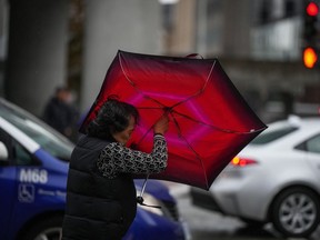A woman struggles with an umbrella in the wind as rain falls in Vancouver, on Monday, Sept. 25, 2023.