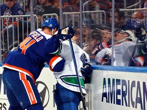Scott Mayfield of the New York Islanders checks Nils Hoglander of the Vancouver Canucks into the glass during the first period at UBS Arena on January 09, 2024 in Elmont, New York.