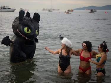 A dragon is seen in the water as three women take a photo during the Polar Bear Swim on New Year's Day at English Bay Beach in Vancouver, B.C., Monday, Jan. 1, 2024.