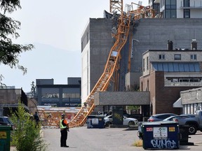 A worker looks on as a police officer investigates a collapsed crane resting on the building it damaged in Kelowna, B.C., Monday, July 12, 2021. The crane was being used on the building site of the 25-storey Brooklyn at Bernard Block residential tower, currently under construction.