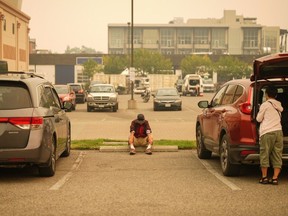 A man sits in the parking lot outside an evacuation centre for those forced from their homes due to wildfires, in Kelowna last August.