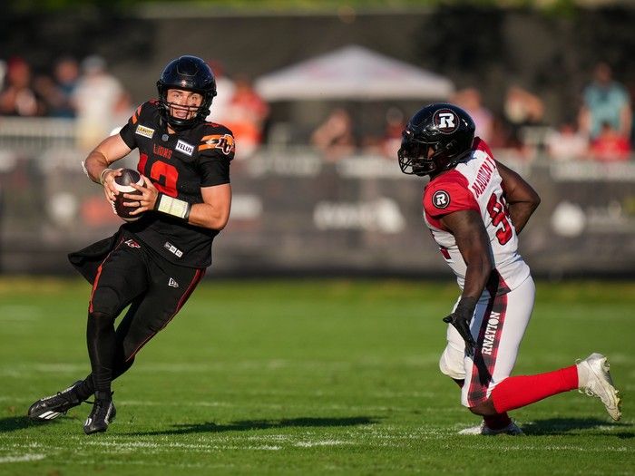 B.C. Lions quarterback Nathan Rourke, left, runs with the ball before completing a pass as Ottawa Redblacks' Lorenzo Mauldin IV watches during the second half of a CFL football game, in Victoria, B.C., on Saturday, August 31, 2024.