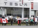 Approximately two dozen people protest outside the Tesla dealership in Langley, March 22, 2025.