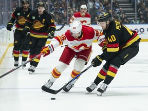 Joel Farabee of the Calgary Flames tries to fight off the check of Elias Pettersson during the first period