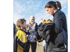 Canadian women's soccer Olympians Christine Sinclair, right, and Kaylyn Kyle sign autographs on a soccer ball for Gary Smith, 8, after getting off a plane in Pinehouse prior to visiting the school there on Monday . Please see story on Page B3.