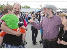 Elijah Day, 3, held by his father Rod Day, left, shyly avoids a fist bump with NDP Leader Thomas Mulcair, with his wife, Catherine, during a Stampede breakfast in Calgary on Saturday. If elected prime minister, Mulcair promises to provide $15-a-day child care and increase the hourly federal minimum wage to $15.