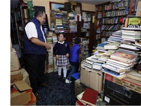 In this Aug. 19, 2015, photo, Jose Alberto Gutierrez, left, talks to children visiting his library at his home in Bogota, Colombia, Wednesday. The reading material slowly piles up, and now the ground floor of his small house is a makeshift community library stacked from floor to ceiling with some 20,000 books, ranging from chemistry textbooks to children’s classics. (AP Photo/Fernando Vergara)