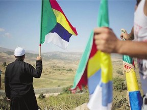 A member of the Druze minority waves the Druze flag as fighting between forces loyal to Bashar Assad and rebels in the Druze village of Khader in Syria continues.