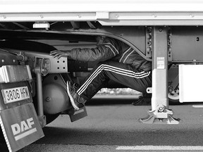 A migrant sits under the trailer of a vehicle as he attempts to cross the English Channel, in Calais Wednesday. Trains and ferry services between Britain and France resumed Wednesday but there were still some disruptions of service.