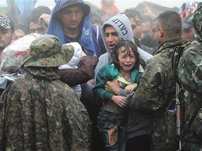 Migrants and refugees wait in the rain to cross the Greek-Macedonian border near the village of Idomeni, in northern Greece Thursday.