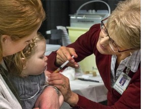 Tara Anderson holds her daughter Charlotte while receiving a flu shot from public health nurse Joan Kirkpatrick during opening day of flu vaccine season at Prairieland Park.