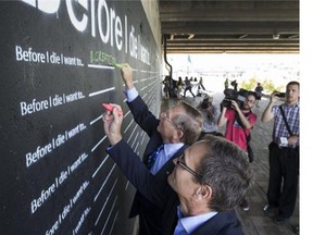 Saskatoon mayor Don Atchison and Lorne Wright write on the new artwork under thew Sid Buckwold Bridge after the announcement that Phase One and Two of River Landing that is now complete, June 23, 2015. The painted wall is to help spruce up the darker walkway.